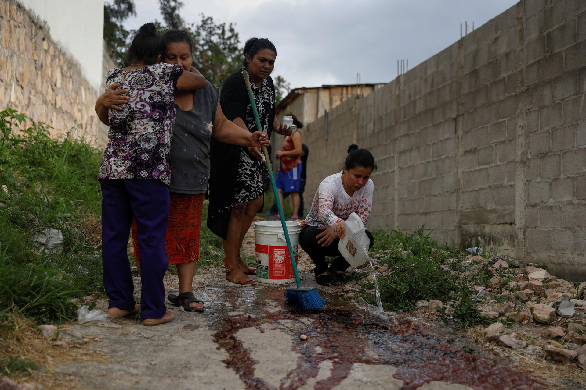 Relatives and friends of Ronald Blanco are shown in the street, a pair hugging and another wash the blood from the crime scene.