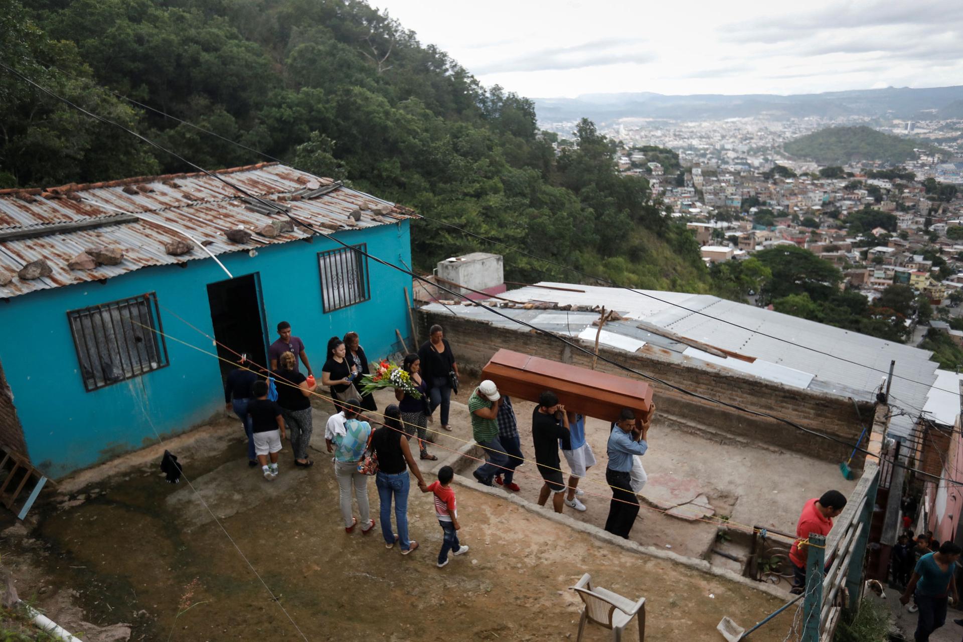 Relatives and friends of Ronald Blanco are shown walking out of a blue house on a hill overlooking Tegucigalpa, carrying his coffin.