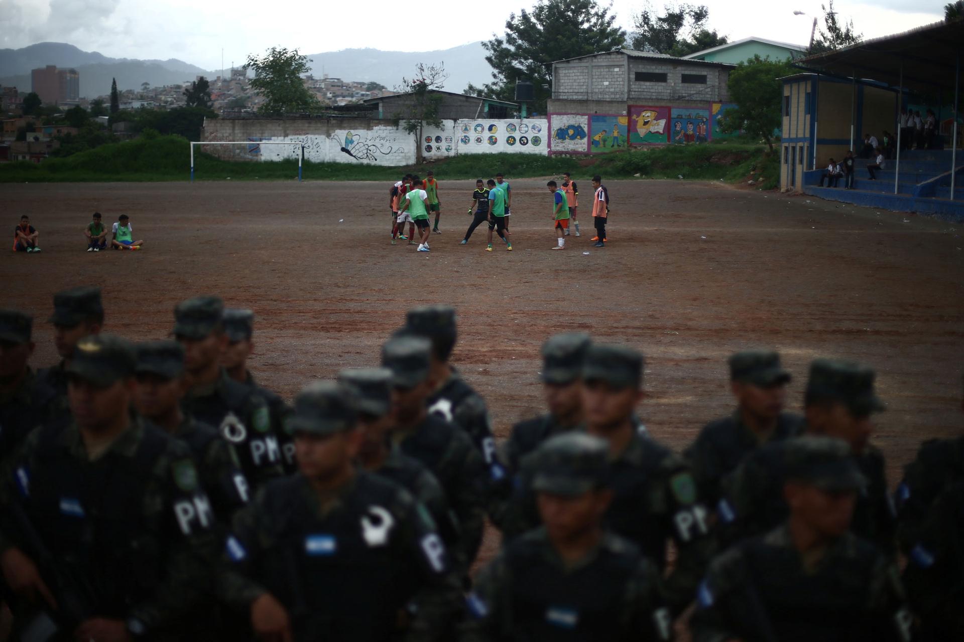 A group of people play soccer in the distance as soldiers are shown in the near ground lined up.