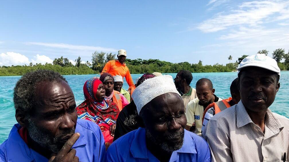 A group of Tanzanians wearing bright colorful clothes ride in a boat.