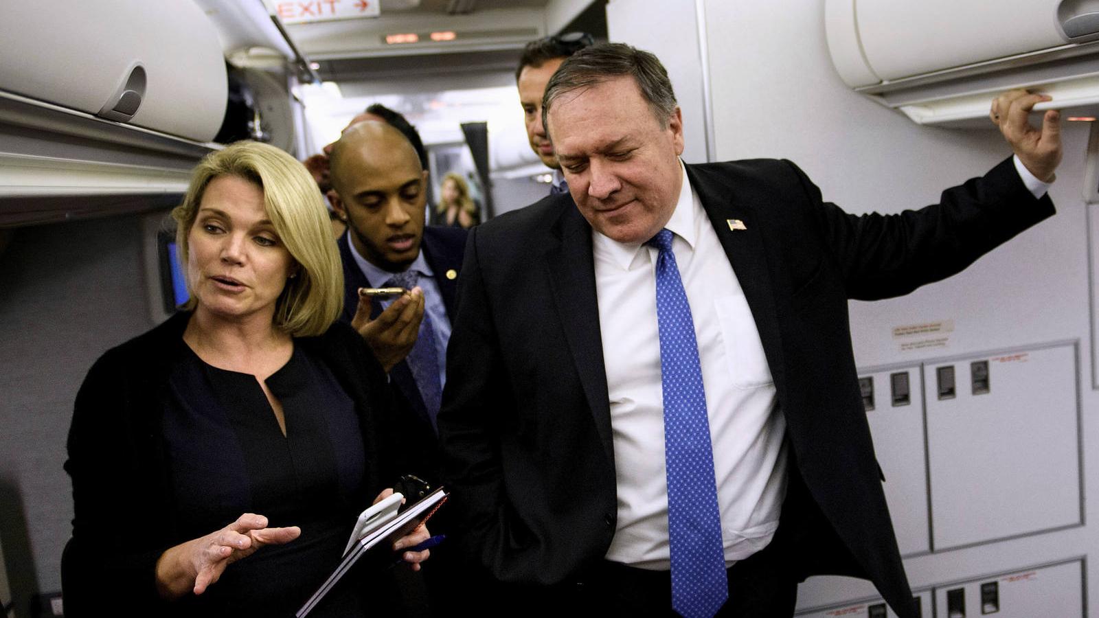 Heather Nauert and Mike Pompeo wear navy blue suits and speak with reporters inside a plane. 