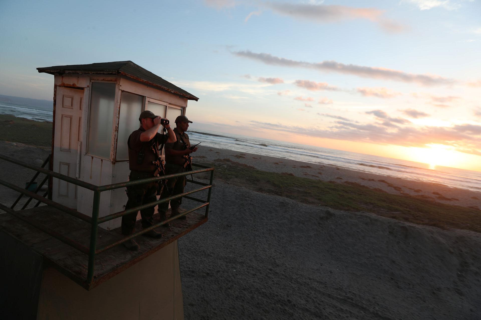 Two policemen look out from a watchtower — one looking through binoculars — at the Chilean and Peruvian border.
