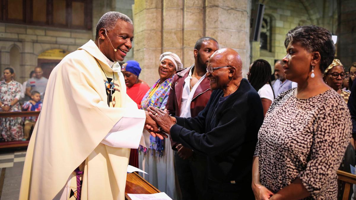 Archbishop Emeritus Desmond Tutu shakes hands with priests inside a church.