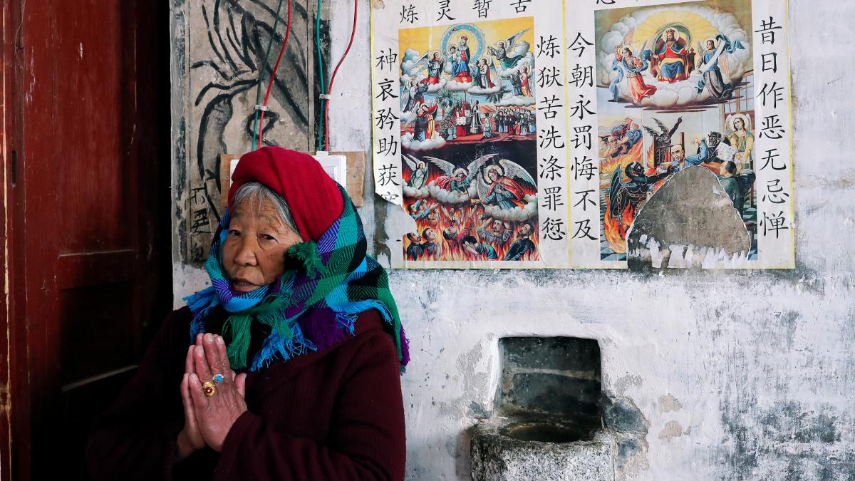 An elderly Tibetan woman prays inside a church in front of religious photos with captions in Mandarin.