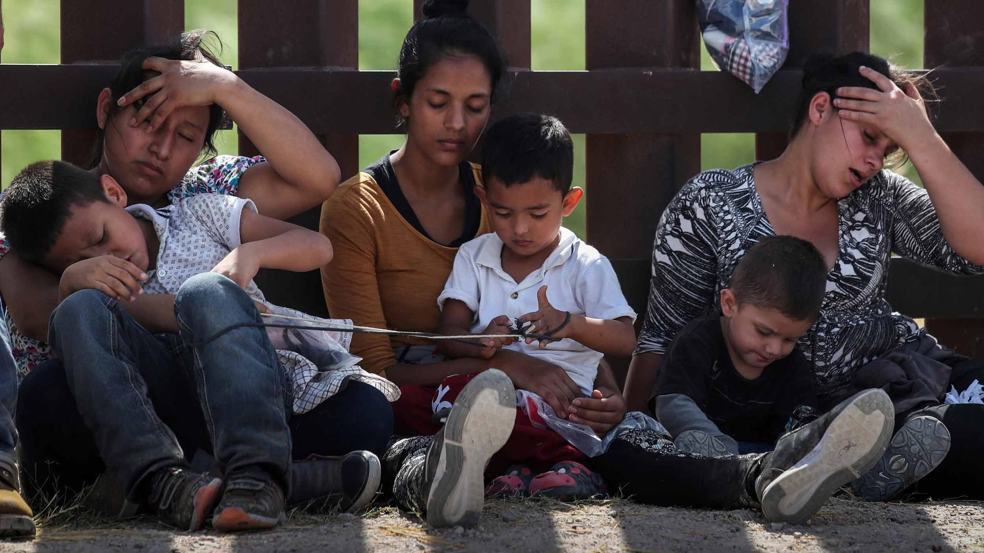 Three women rest against a fence with their children in their laps