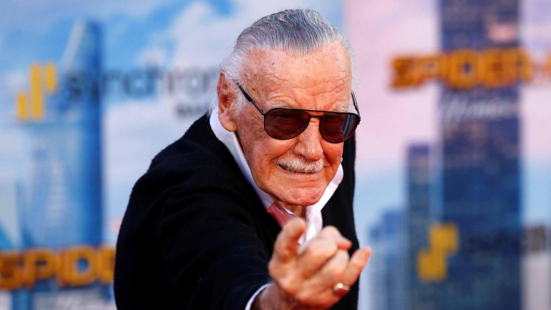 Stan Lee poses like Spiderman shooting a web from his wrist