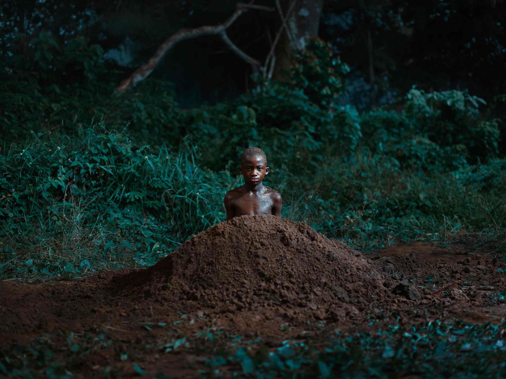 A boy is centered in the frame, inside a small mound, like mole
