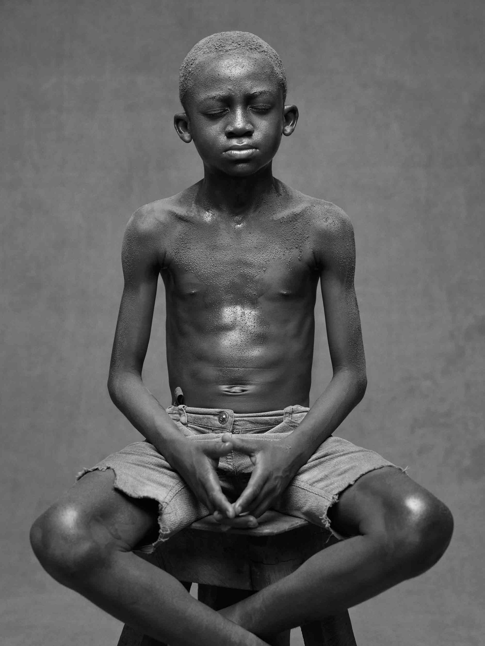 A boy poses for a photograph with his fingers touching and his ankles crossed