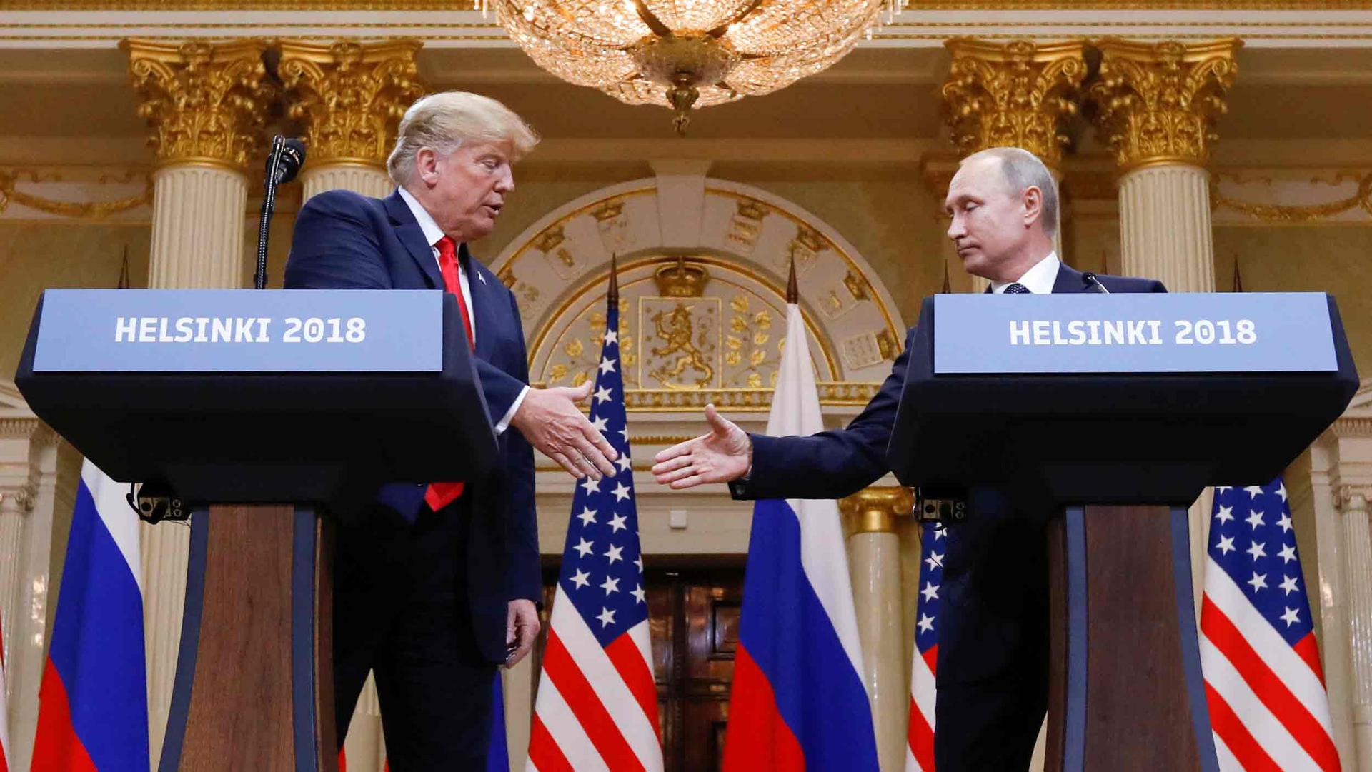 Donald Trump and Vladimir Putin shake hands behind two podiums reading Helsinki 2018