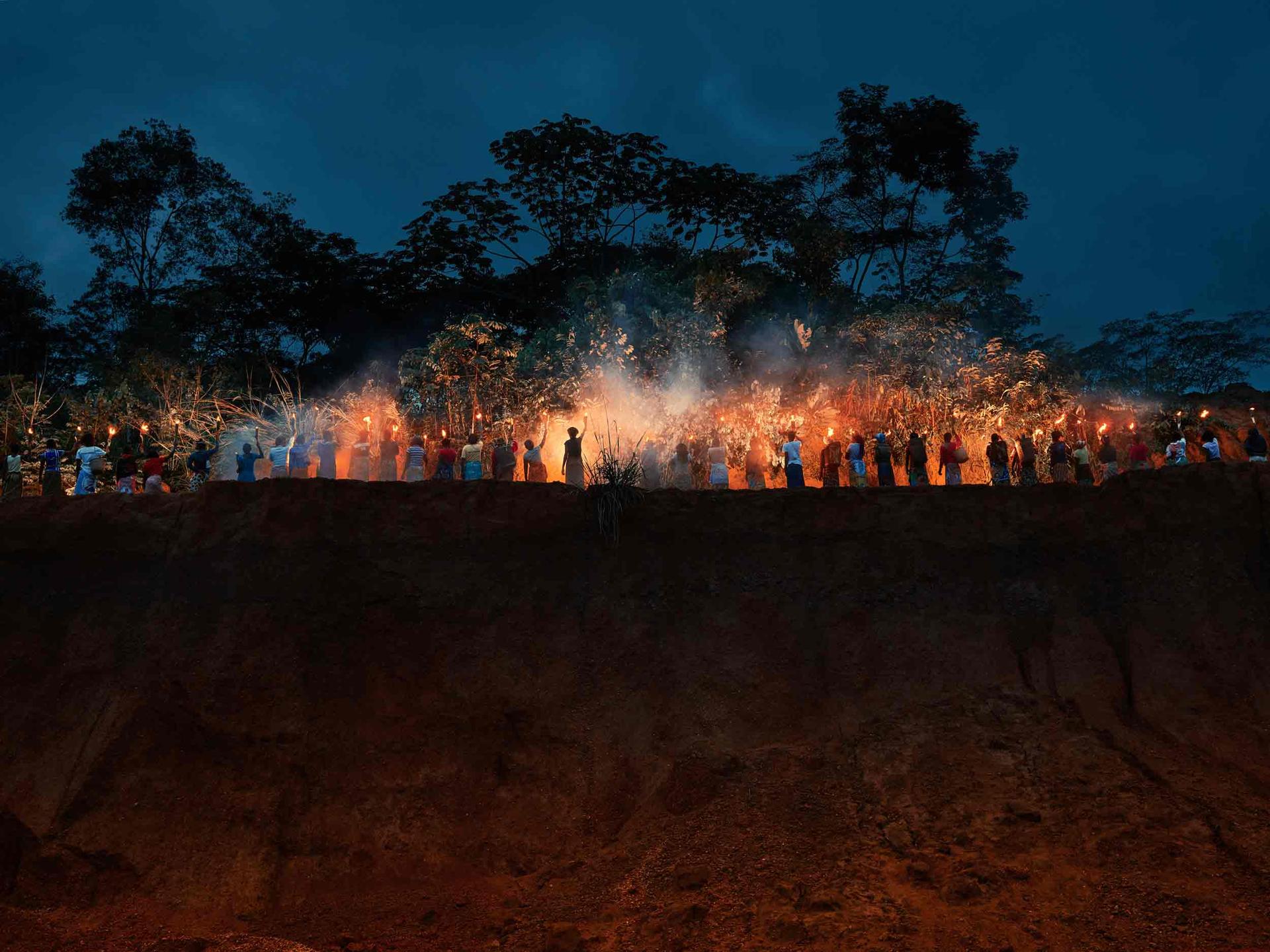 Women stand in a line each holding a torch of fire along a cliff