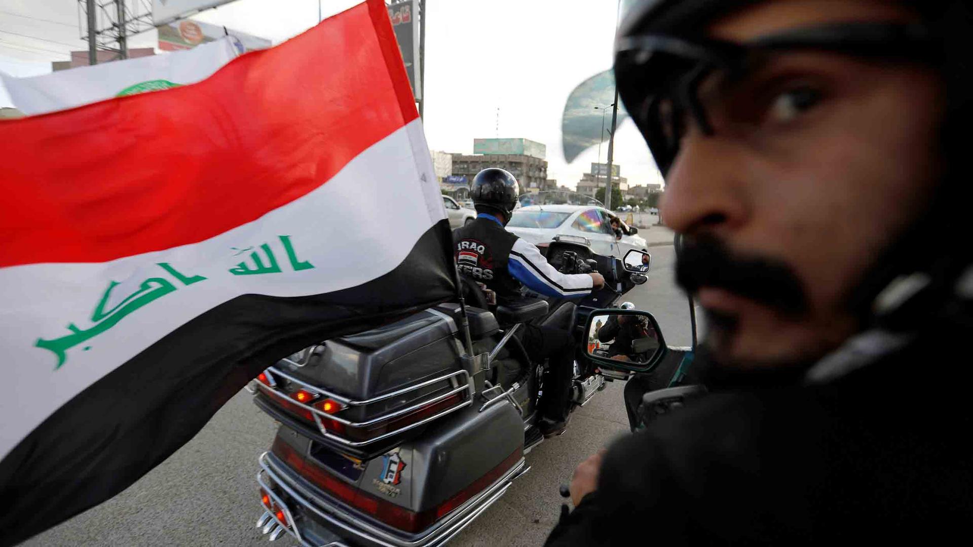 An Iraqi flag blows in the wind from the back of motorcycle.
