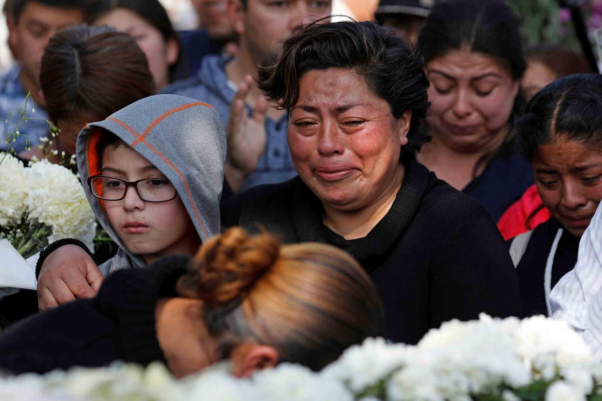 A woman cries and hold onto a young boy as a crowd of people gather for a funeral