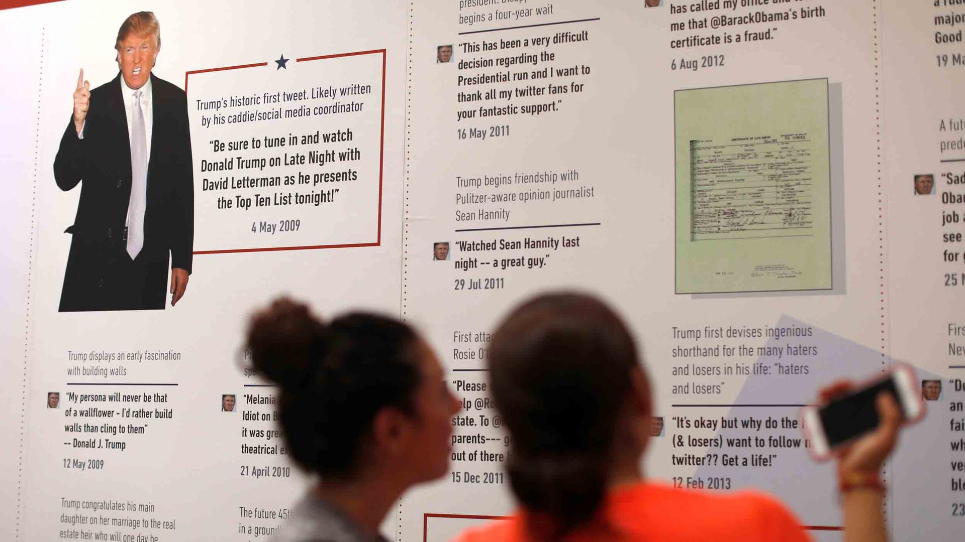 Two people look at a museum displaying showing a history of Donald Trump's tweets