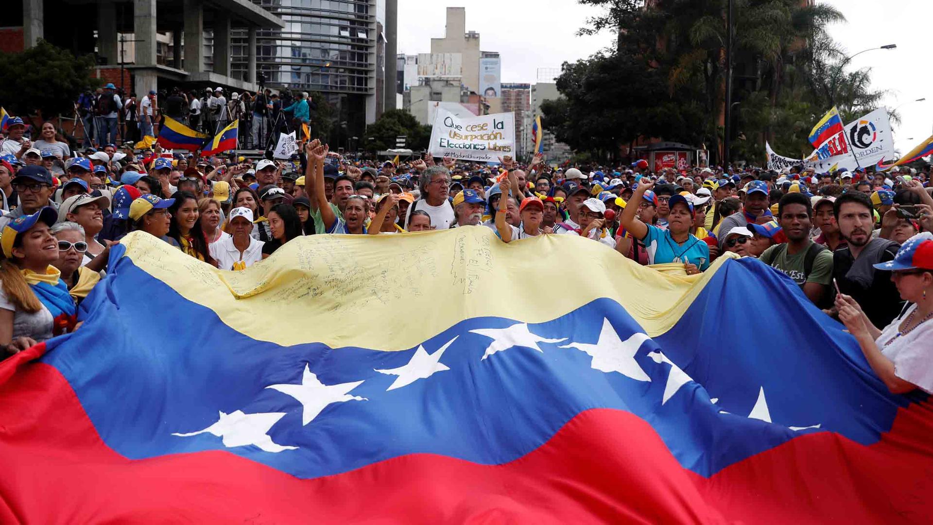 Hundreds of protests stand behind a massive Venezuelan flag