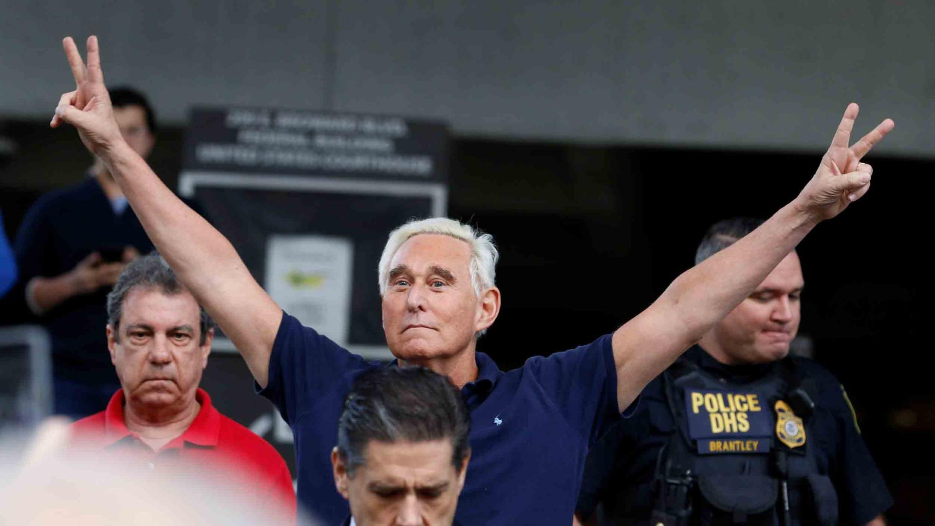 Roger Stone puts his hands up and makes peace signs as he walks to microphones