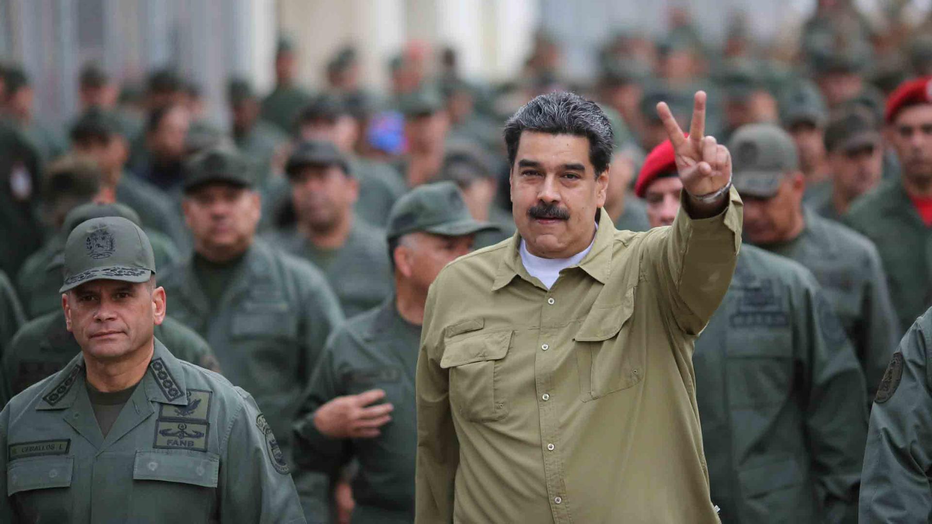Nicolas Maduro holds up two fingers as he is surrounded by men in military uniforms.
