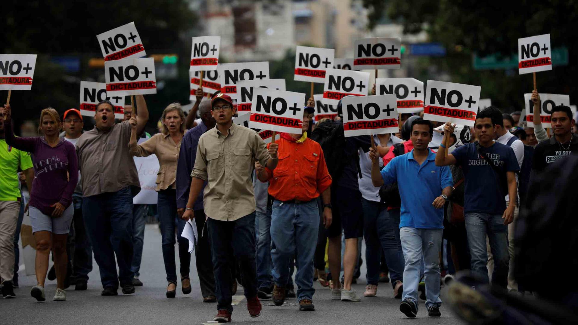 A group of people hold signs that say "No dictadura" as they march down a street.