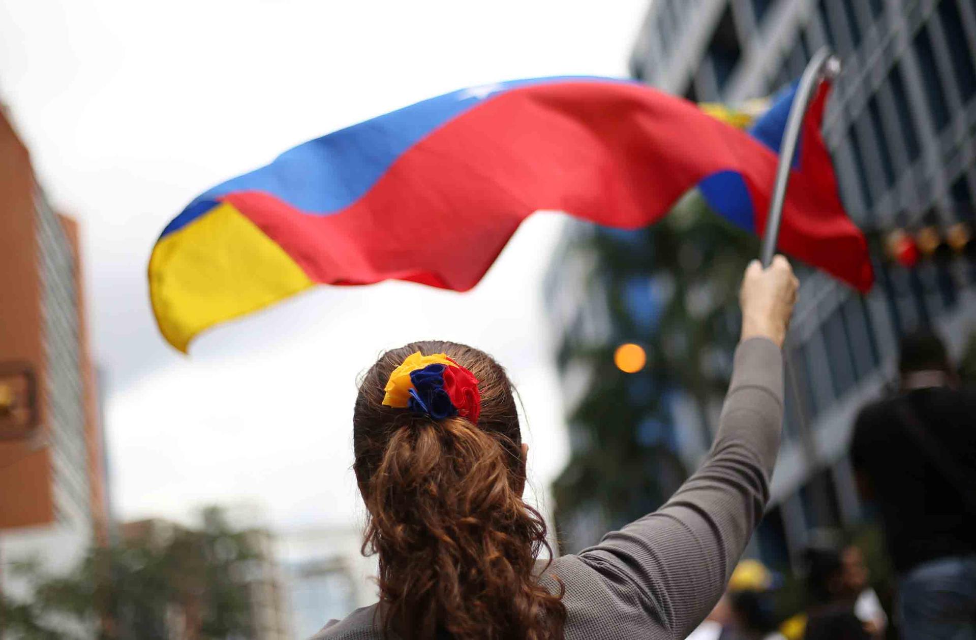 A woman stands with her back to the camera and waves a Venezuelan flag in front of her