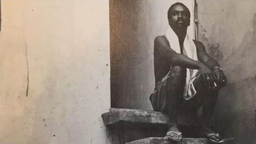 An African American man sits on a stair step with a towel around his neck
