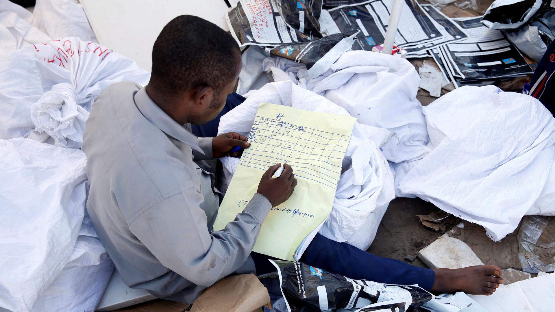 a man without shoes, sits on a big pile of papers while he examines voting materials 