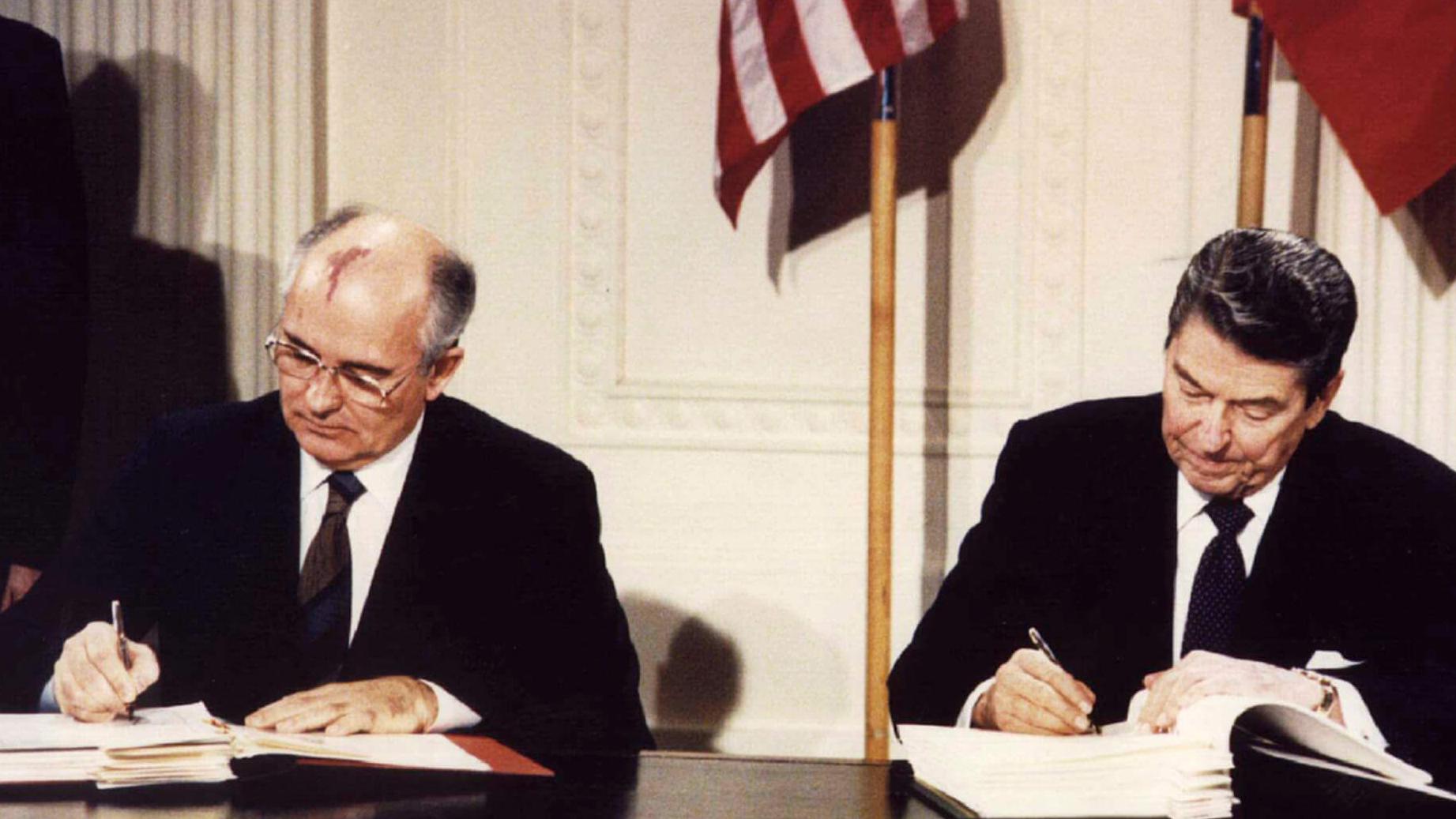 Two leaders sit at a desk signing a document. 
