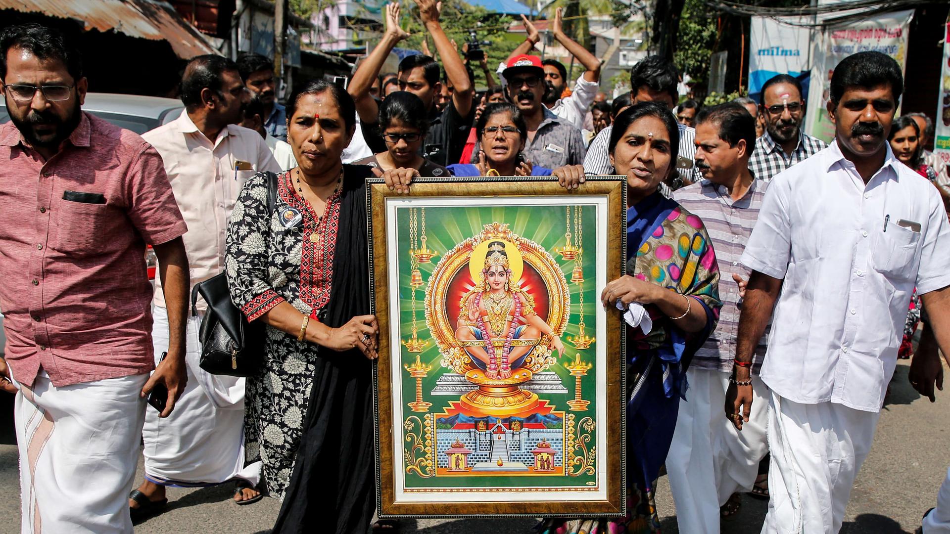 Protesters walk down the street carrying a sign of a Hindu deity. 