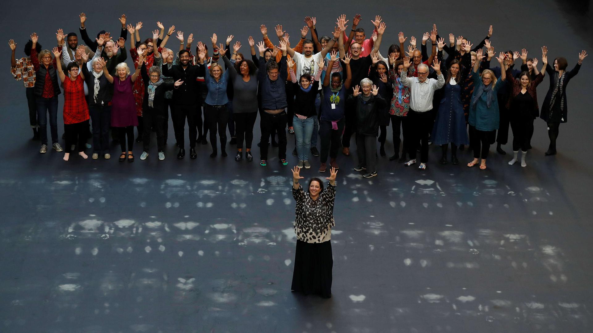 Cuban artist Tania Bruguera stands with her arms in the air, and dozens of people behind her, standing in the same position 