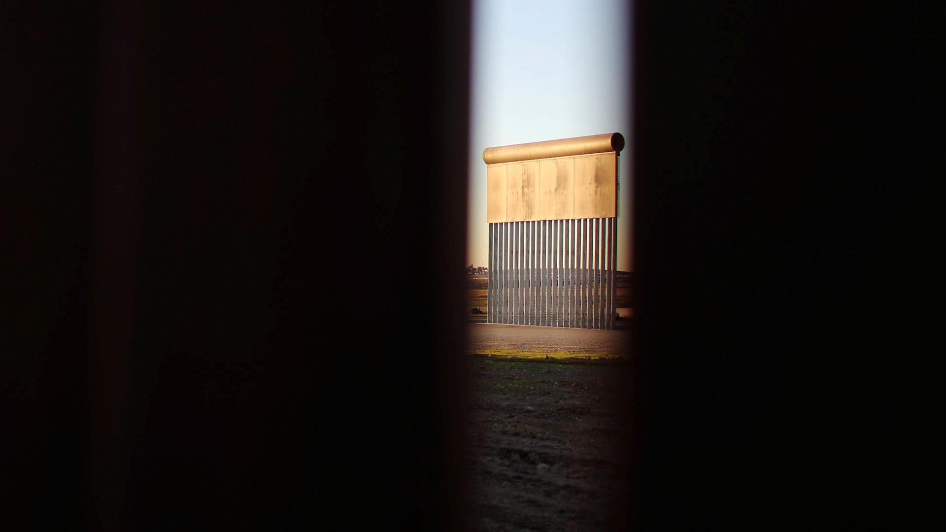 A slatted metal prototypes of a border wall is shown, photographed through the border wall in Tijuana, Mexico.