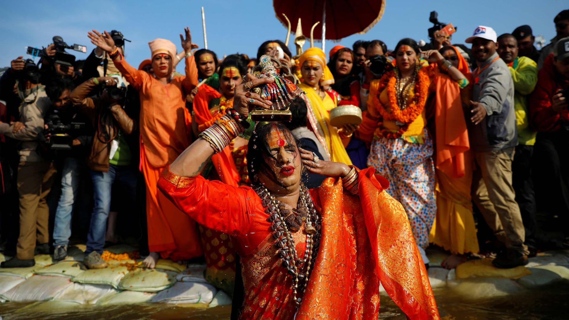 A transgender Indian woman in an orange sari with wet hair in front of a crowd