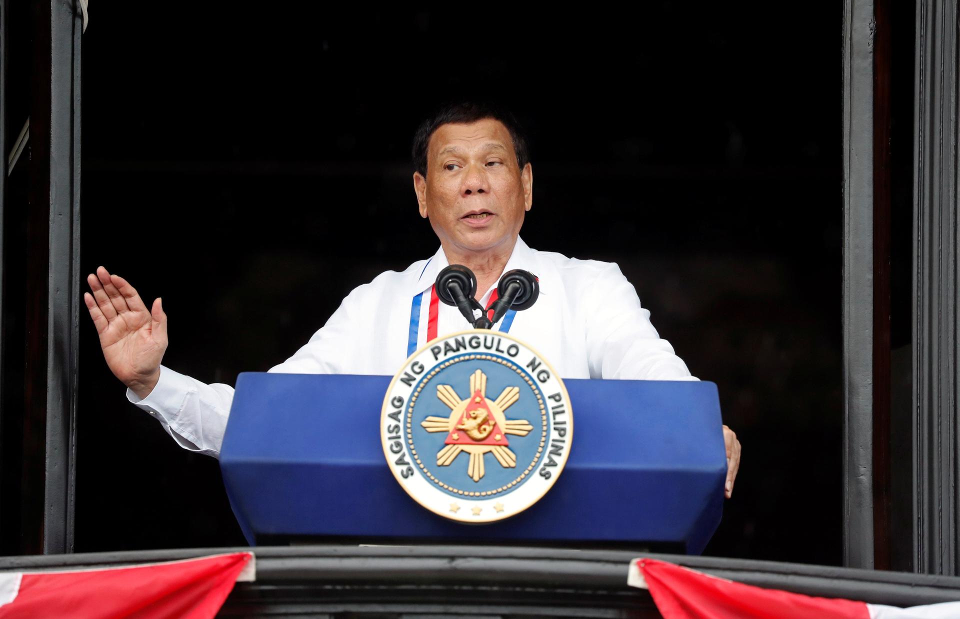 Philippine's President Rodrigo Duterte speaks behind a blue podium in a white shirt 