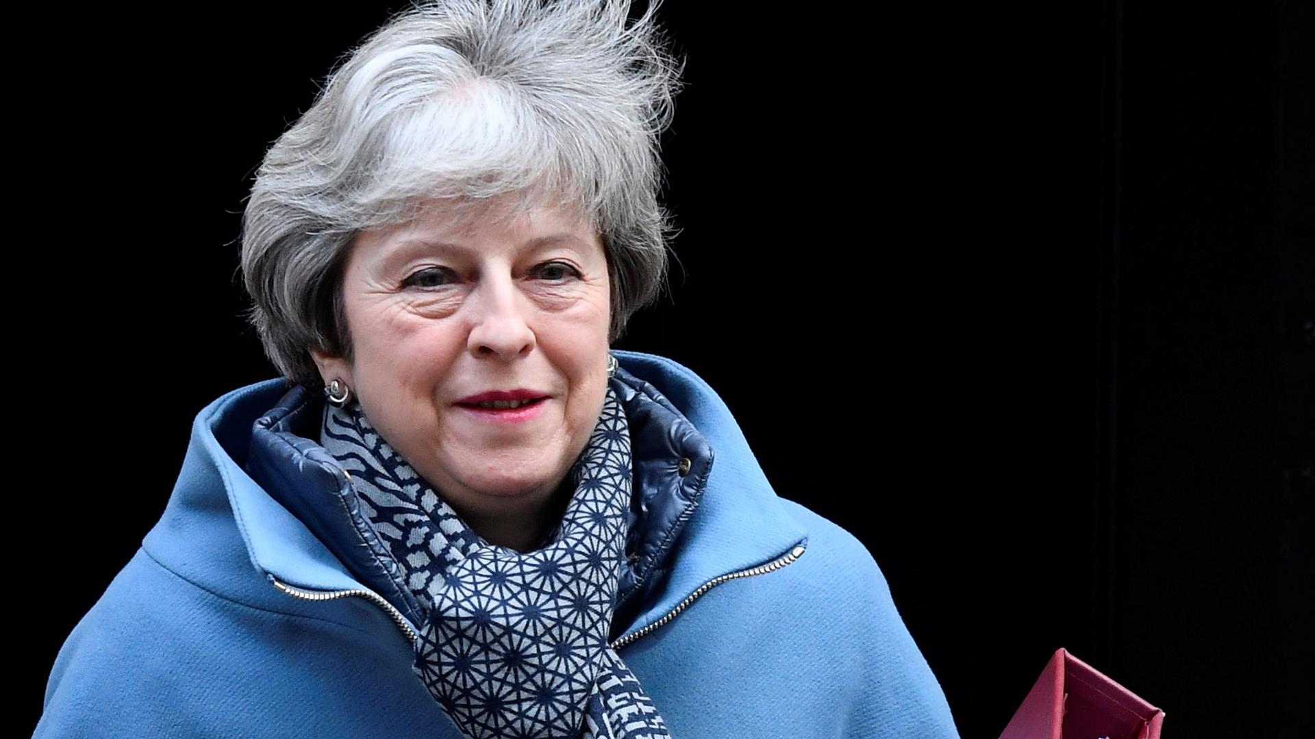 Britain's Prime Minister Theresa May shown leaving Downing Street wearing a blue jacket and scarf while carrying a red binder.