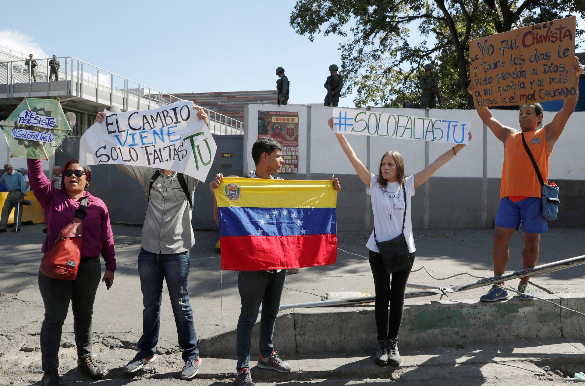 several people hold signs outside the walls of a military outpost 
