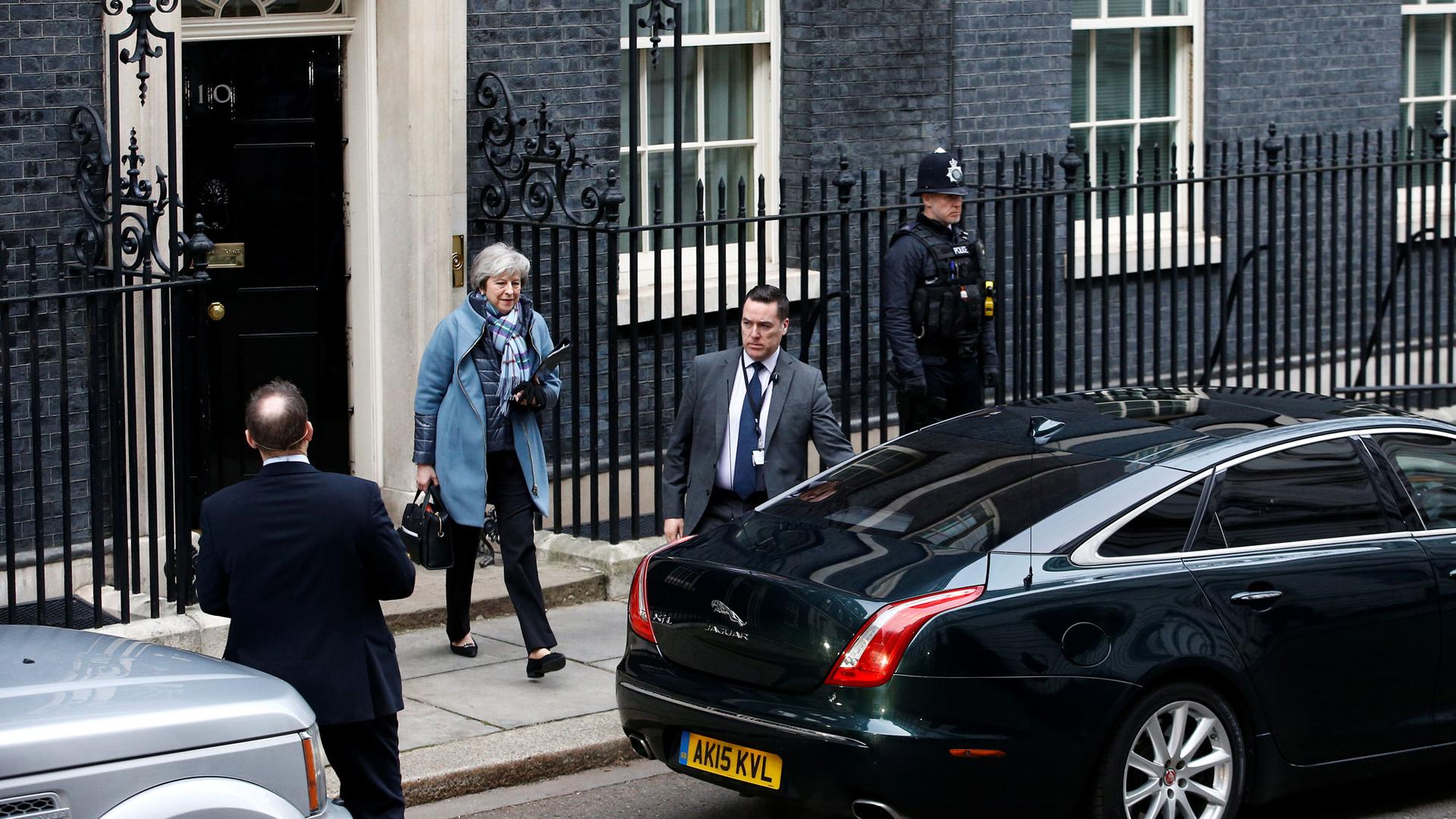 Britain's Prime Minister Theresa May is shown in a blue jacket and scarf walking out of 10 Downing Street to a car.