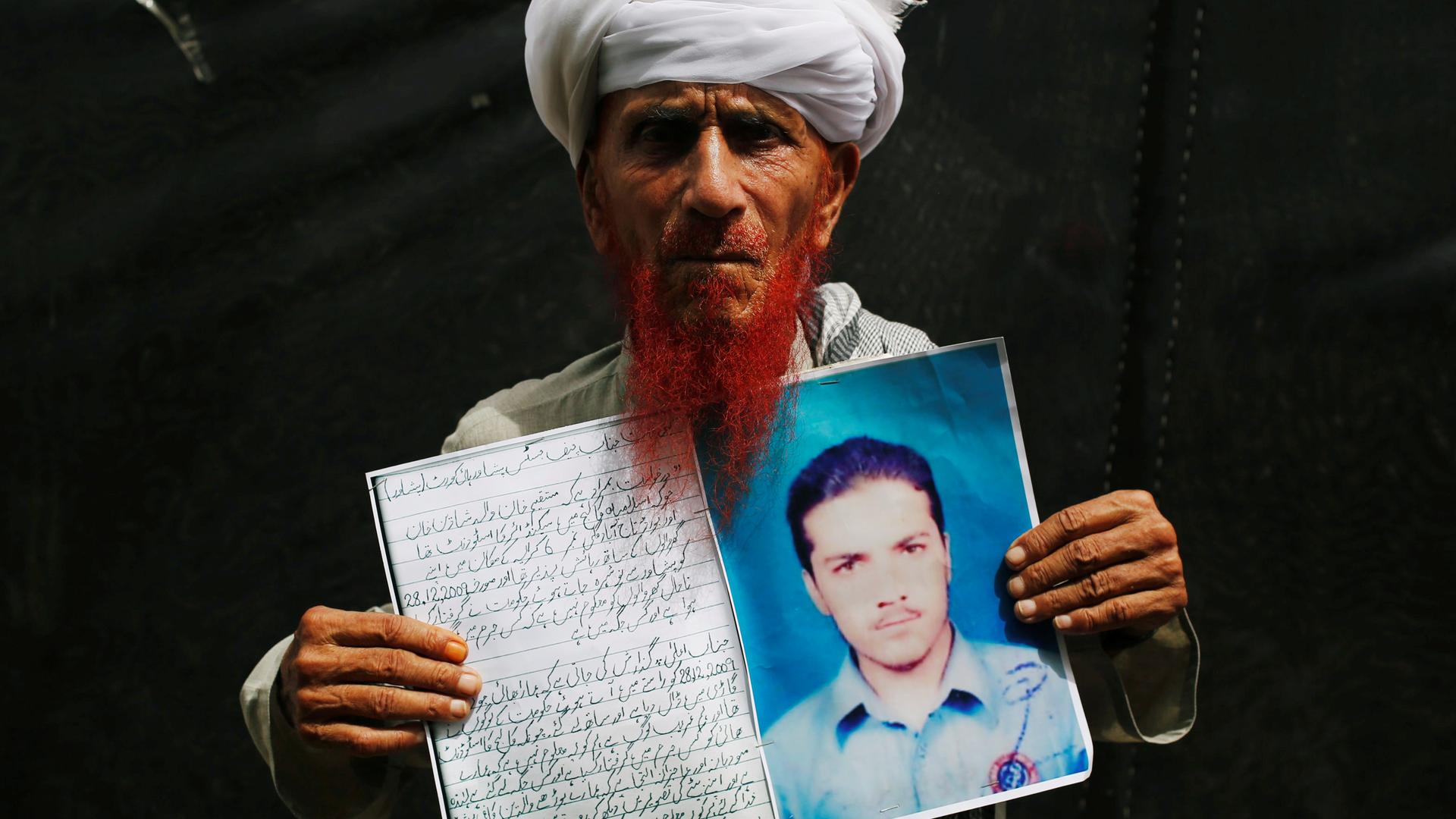 A man in white turban holds photo of his missing son.