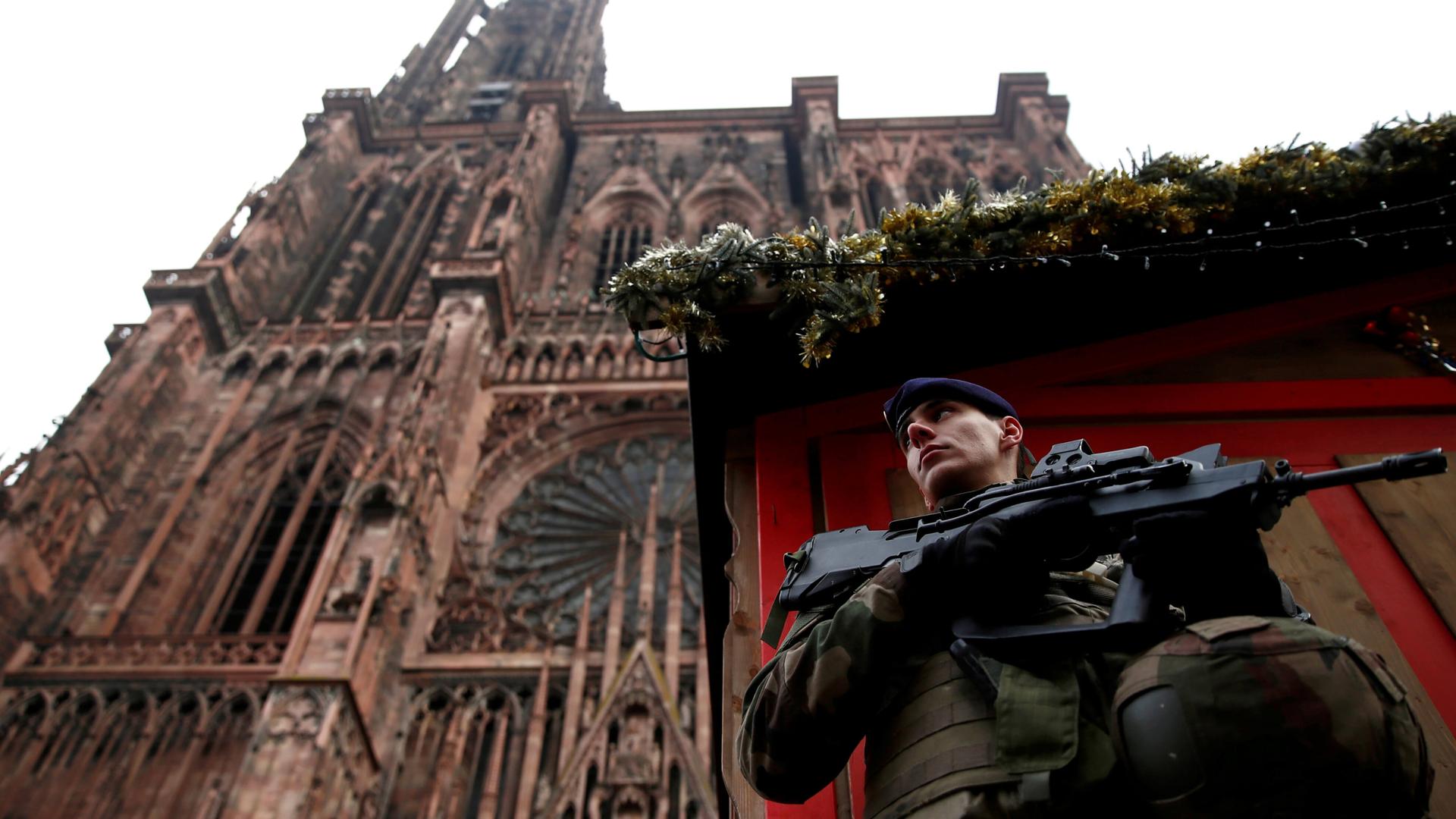 A soldier with a gun stands guard in front of a looming Cathedral.
