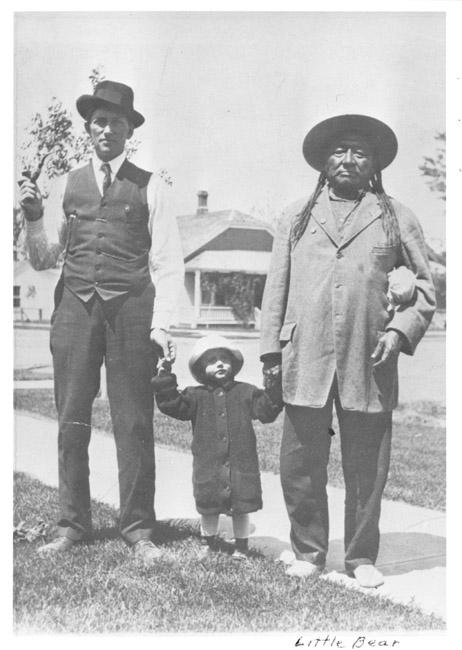 Black and white image of one white man and one Indigenous man holding the hands of a child.