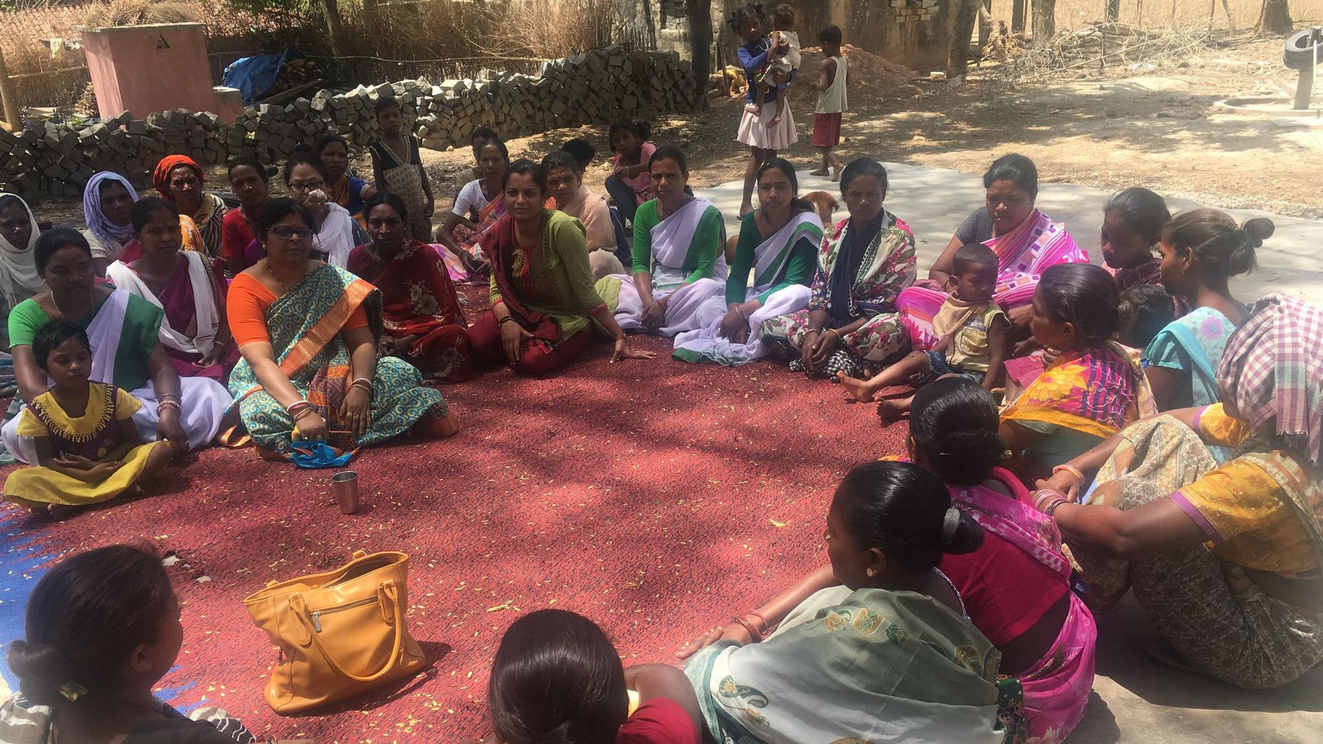 women wearing colorful saris gather in a circle. 