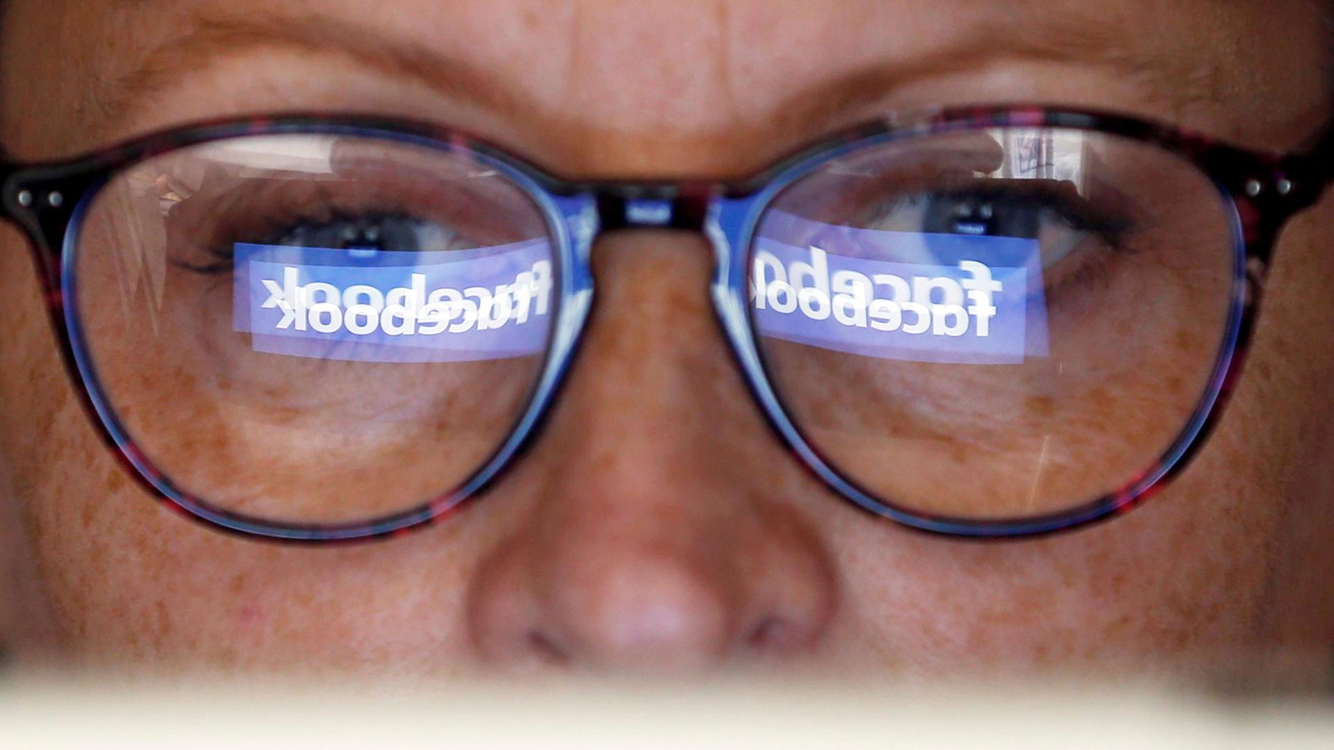 The Facebook logo is reflected in the lenses of a woman's glasses