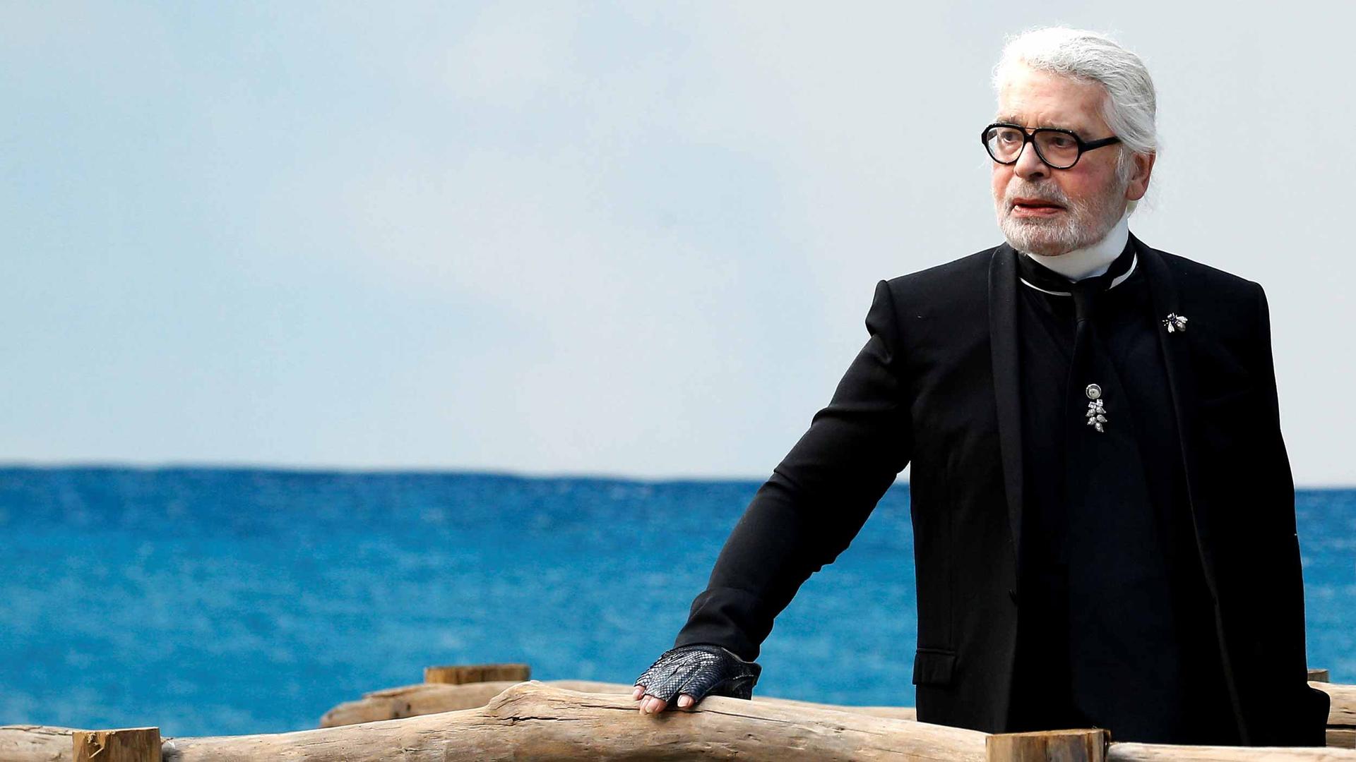 German designer Karl Lagerfeld stands before an ocean backdrop at a fashion show.
