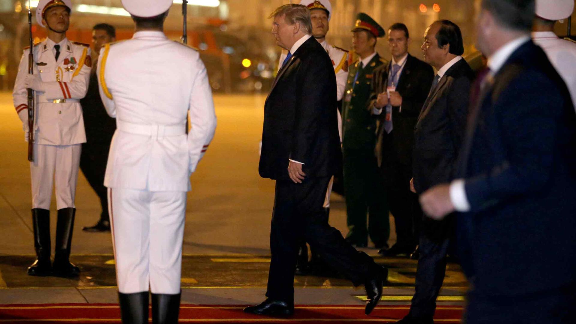 US President Donald Trump walks on a red carpet flanked by Vietnamese military wearing white uniforms.