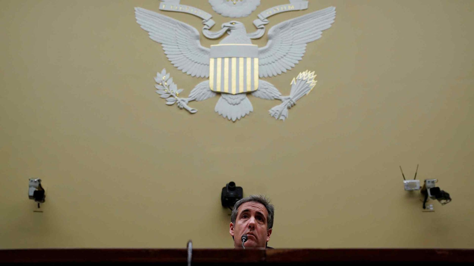 Michael Cohen, Trump's personal lawyer, sits in front of a microphone. Overhead is the US eagle seal. 
