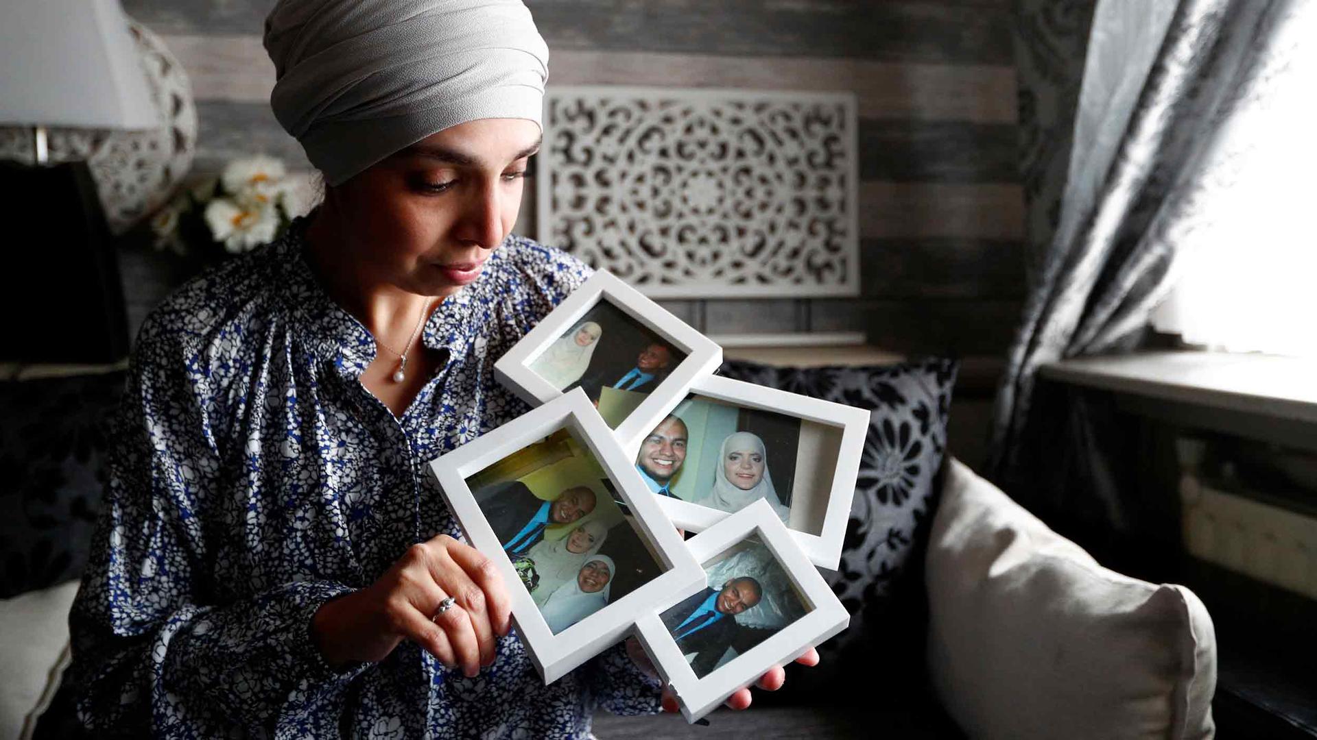A woman holds framed pictures of family members in her hands