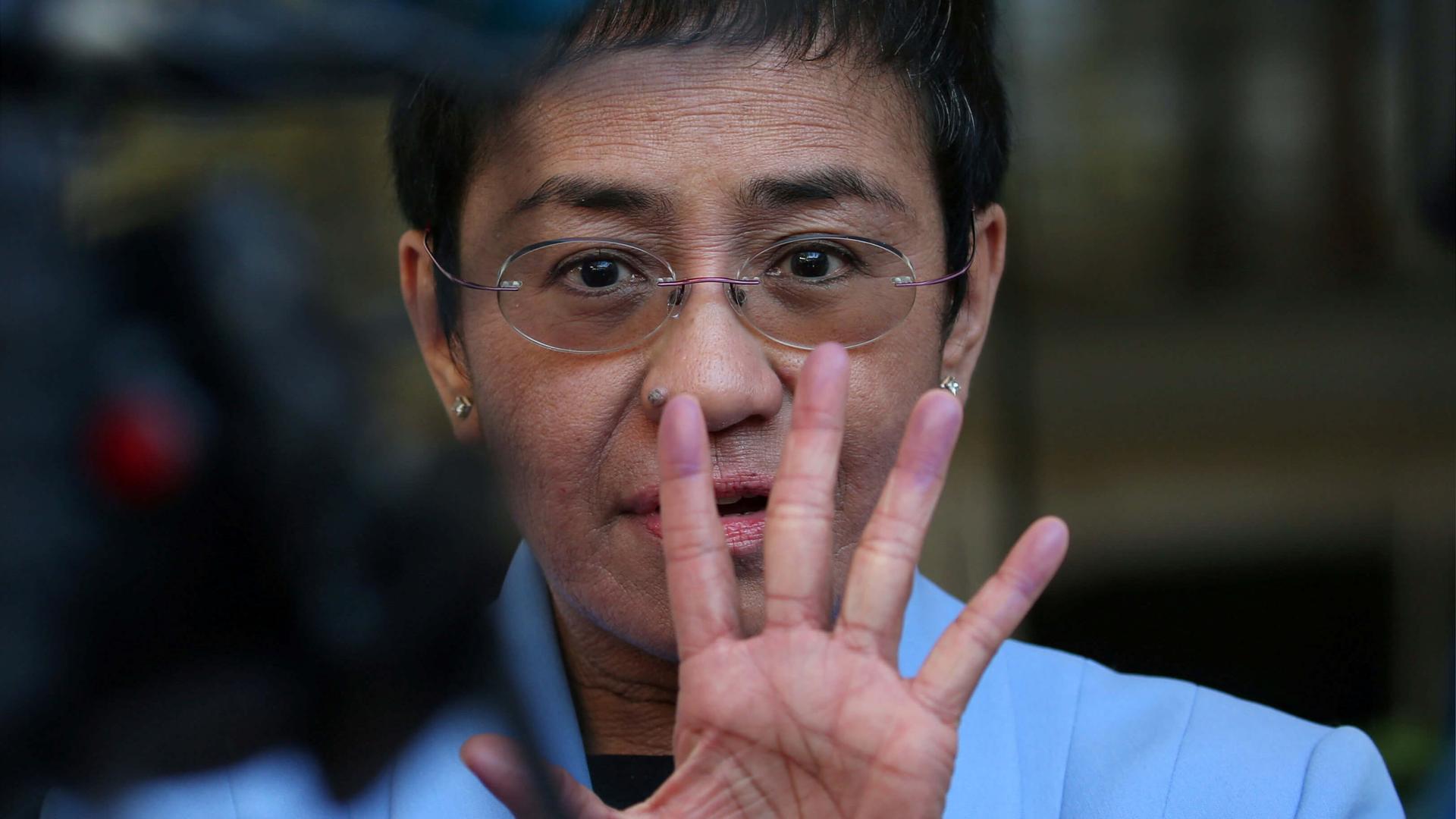 A closeup of Maria Ressa with her hand up in front of her face. 