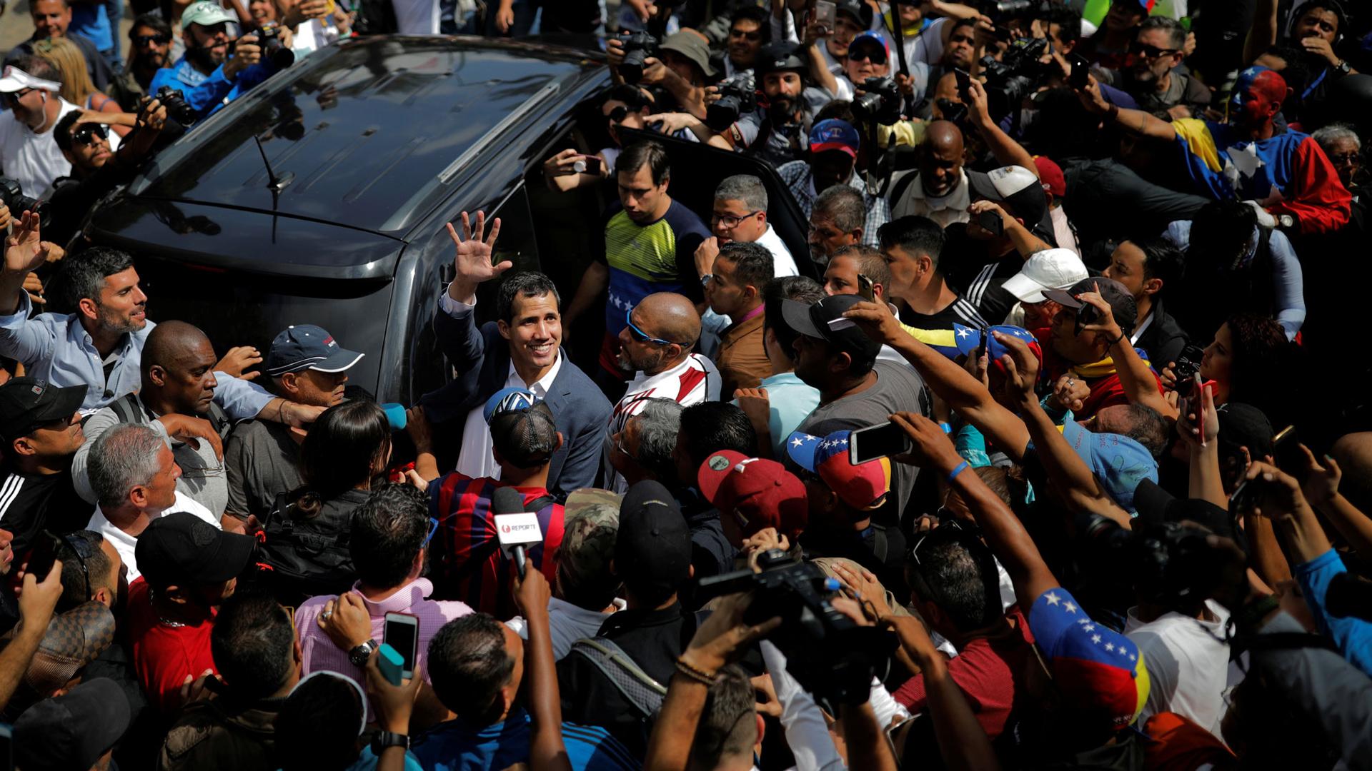 Venezuelan opposition leader Juan Guaido is shown surrounded about people on all sides next to a van. 