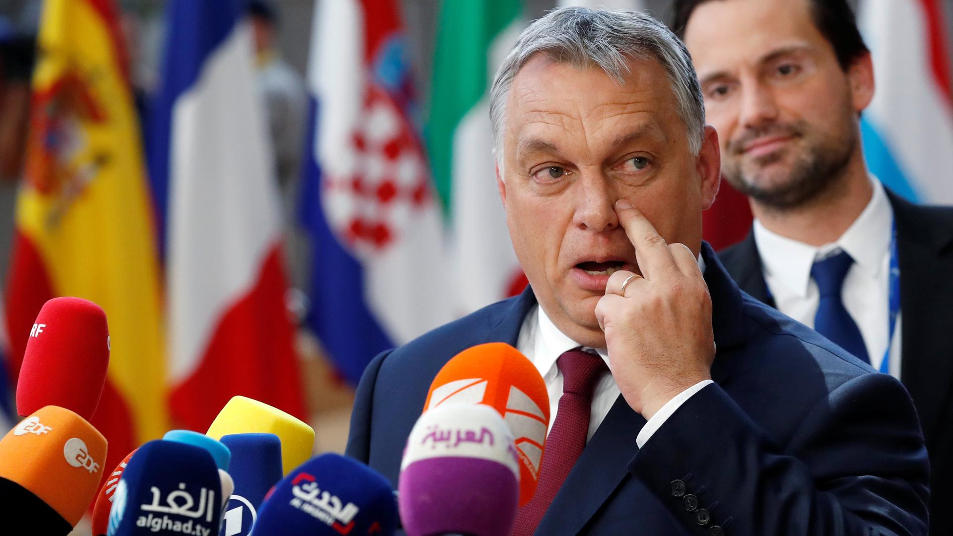 Hungarian Prime Minister Viktor Orbán stands in front of several flags while speaking into several media microphones