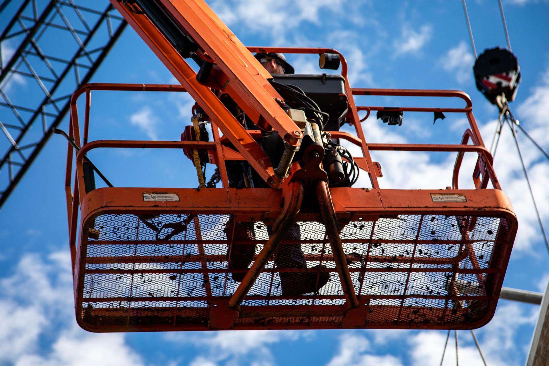 A worker is shown from below standing on an orange platform of a hydraulic crane.