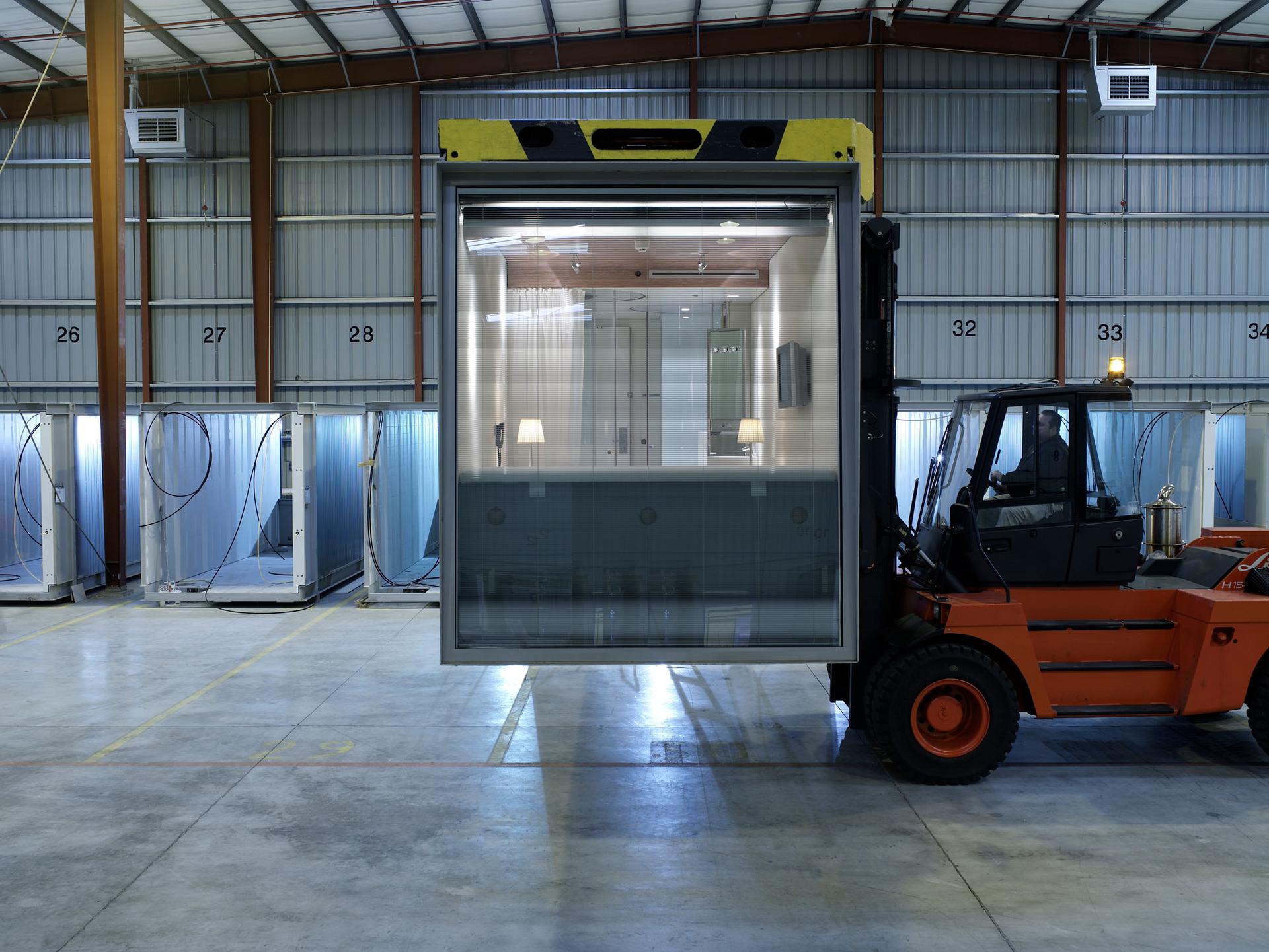 A modular apartment unit from CitizenM is shown on a factory floor being moved using a forklift.
