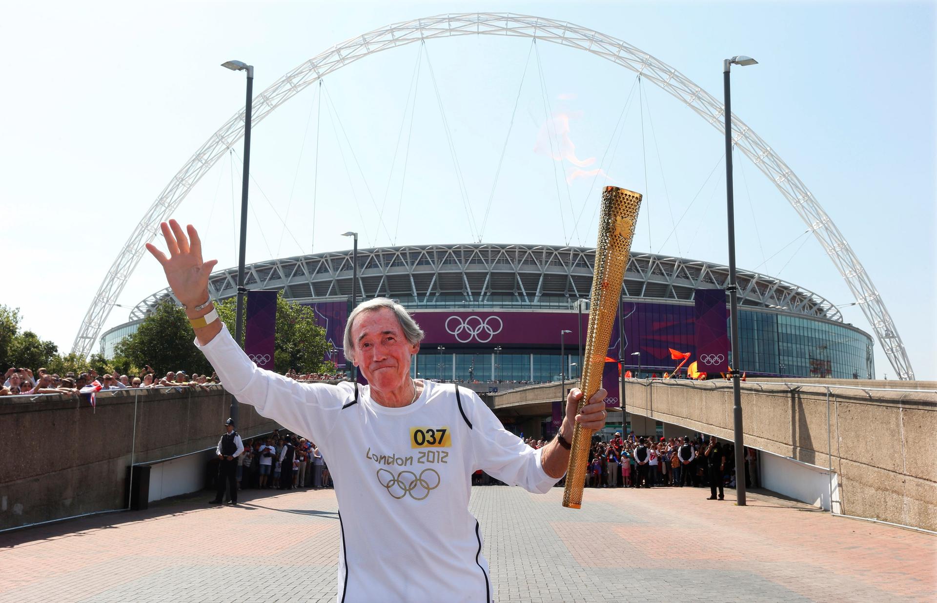 Gordon Banks runs with his arms up, one holding the olympic torch