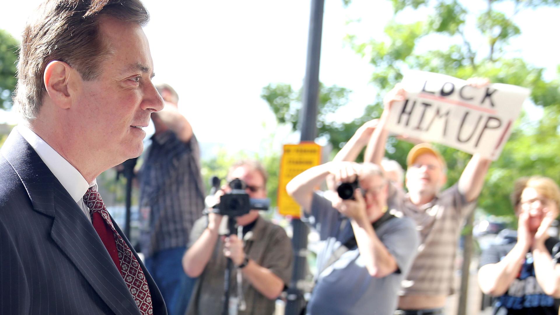 Former Trump campaign chairman Paul Manafort is shown wearing a suit walking past people with cameras.