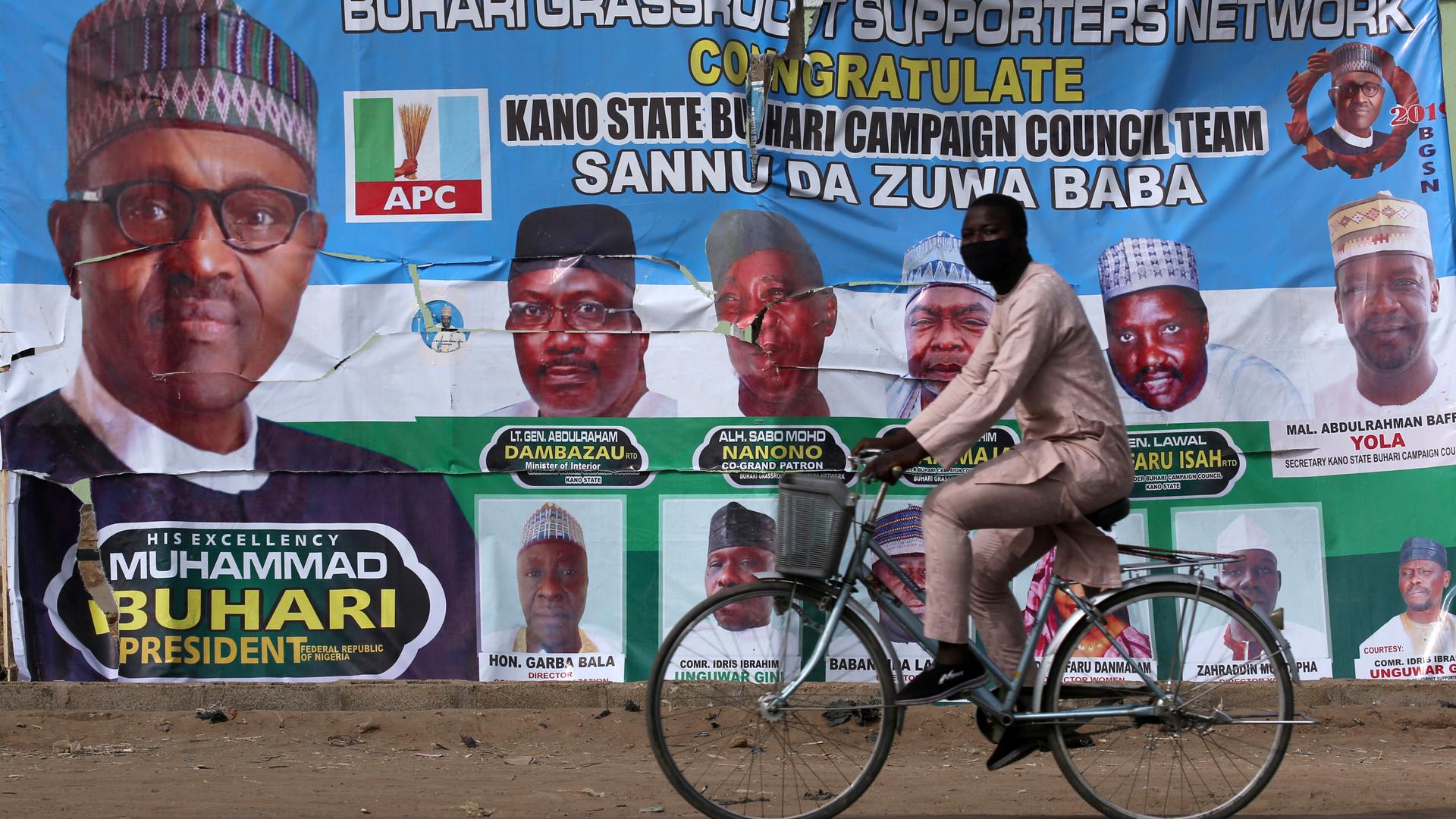 A cyclist drives pasts a campaign poster for President Muhammadu Buhari in a street